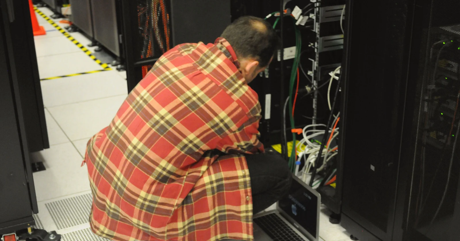 Technician using a laptop while maintaining a server rack